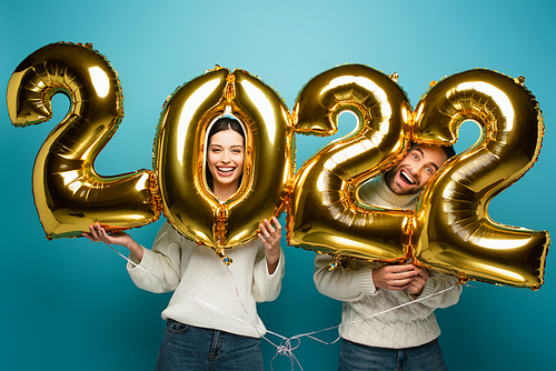 cheerful couple  near golden 2022 balloons on blue