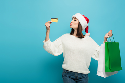 woman in white pullover and santa hat  near credit card while holding purchases on blue