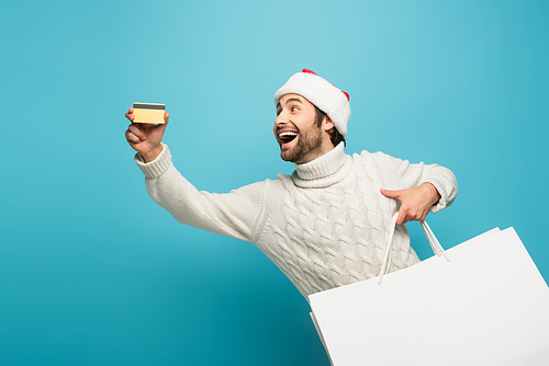 excited man with shopping bags showing credit card on blue