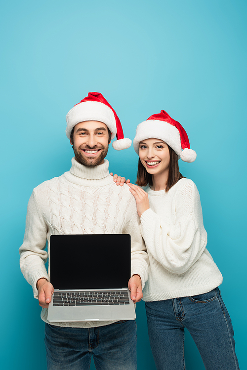 happy man in santa hat holding laptop with blank screen near smiling woman isolated on blue