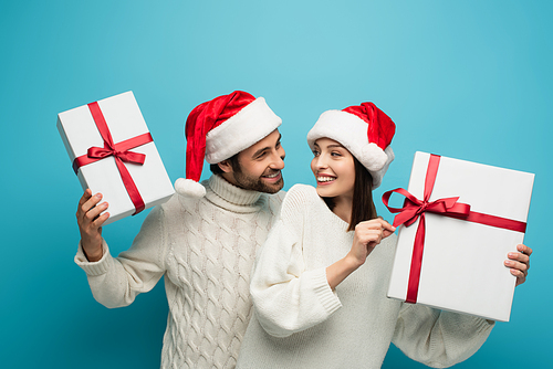 happy couple in santa hats looking at each other while holding shopping bags on blue