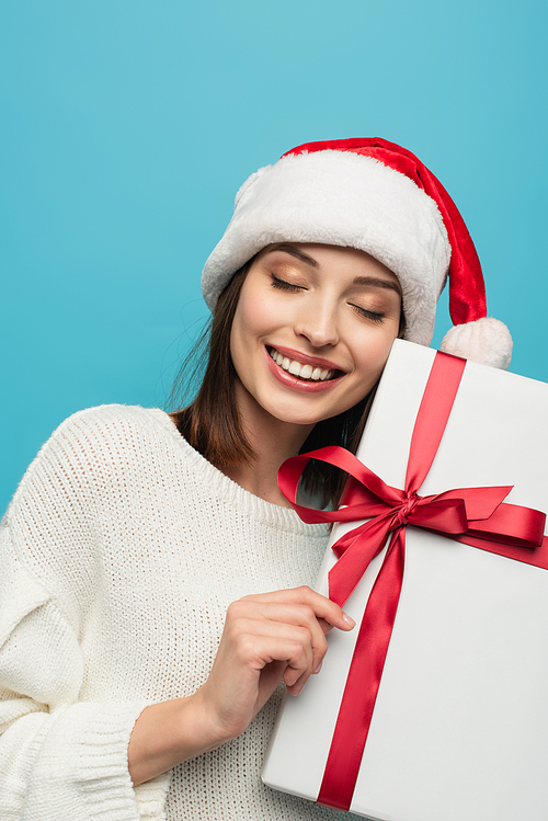 pleased woman in santa hat holding present isolated on blue