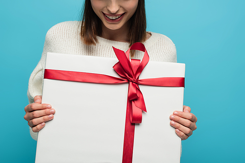 cropped view of smiling woman holding white gift box with red ribbon on blue