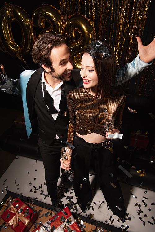 high angle view of happy man and elegant woman with champagne glasses near sparkling decoration on black