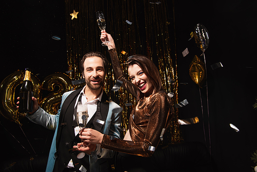 joyful couple with bottle and glasses of champagne  near christmas decoration on black