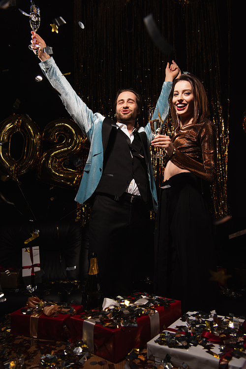 excited elegant couple with champagne glasses  near shiny festive decoration on black