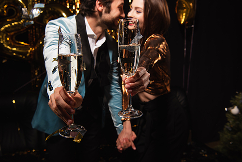 selective focus of champagne glasses in hands of blurred couple celebrating christmas on black