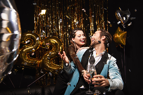 cheerful couple clinking champagne glasses near sparkling christmas decoration on black