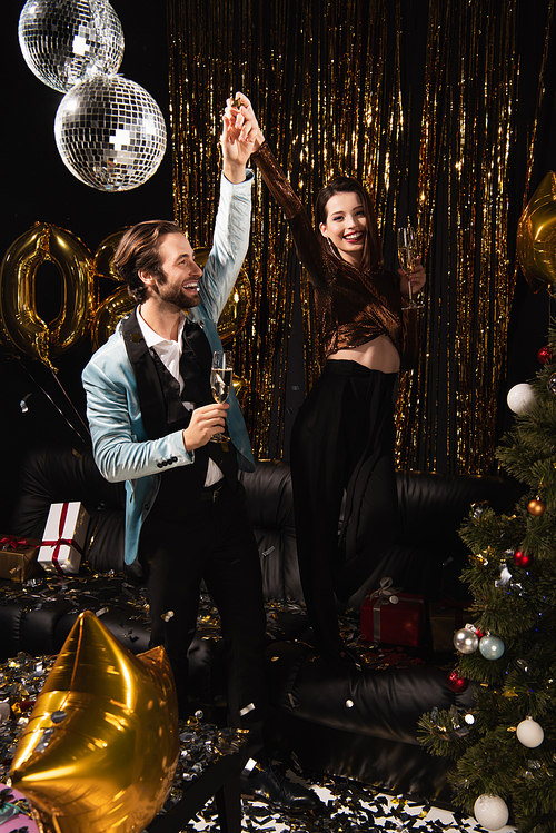 excited couple with champagne glasses holding hands while celebrating christmas on black