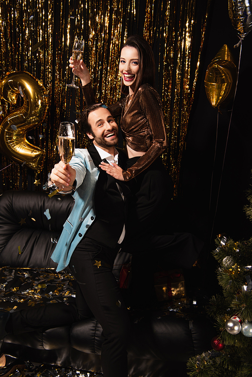 happy couple holding champagne glasses during christmas party on black