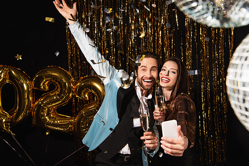 elegant woman taking selfie with excited man while celebrating christmas on black