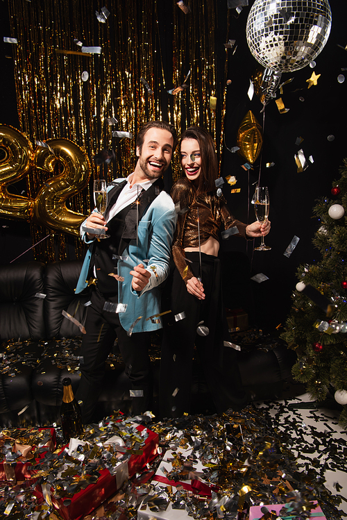 cheerful and elegant couple with sparklers celebrating christmas near shiny decoration on black