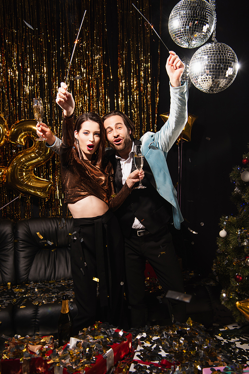 thrilled couple with sparklers and champagne glasses celebrating christmas on black