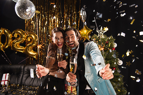 overjoyed couple with champagne and sparklers celebrating new year near shiny decoration on black