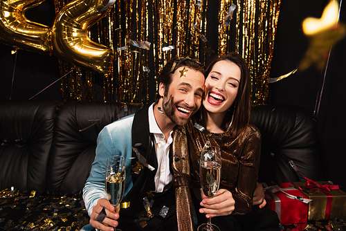 happy couple with champagne glasses celebrating christmas near shiny decoration on black