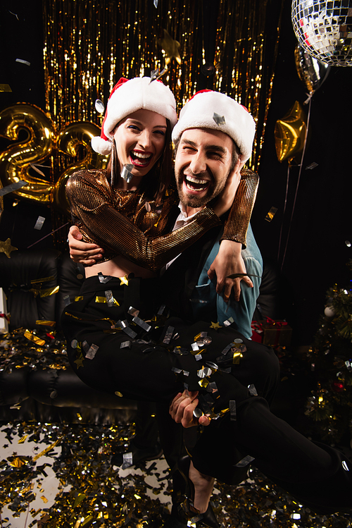 excited man holding cheerful woman in hands while celebrating new year on black