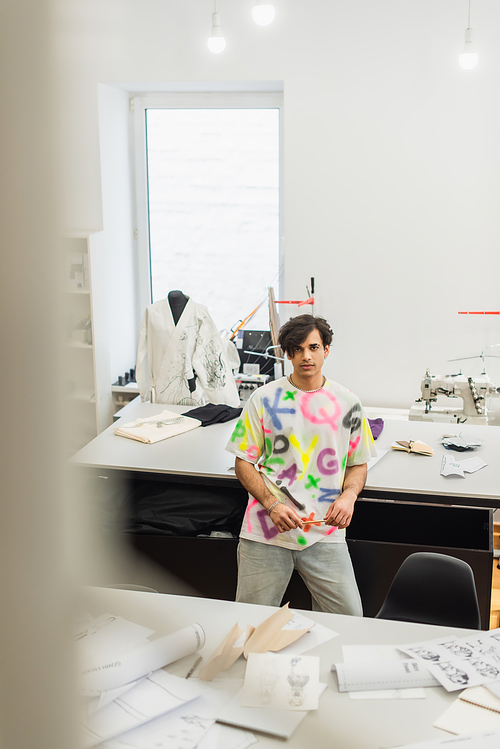 high angle view of trendy fashion designer  near desk with sewing patterns, blurred foreground