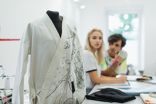 blurred designers looking at kimono with traditional drawing on mannequin in tailor shop