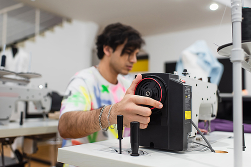 young blurred tailor regulating sewing machine in fashion workshop