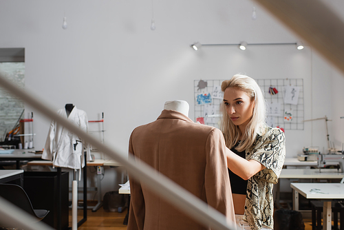 young, blonde fashion designer near mannequin in atelier