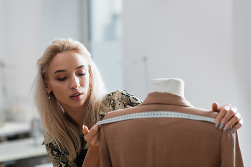 young fashion designer measuring blazer on mannequin in fashion workshop