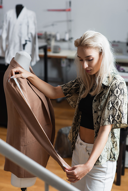 stylish designer measuring blazer on mannequin in fashion studio