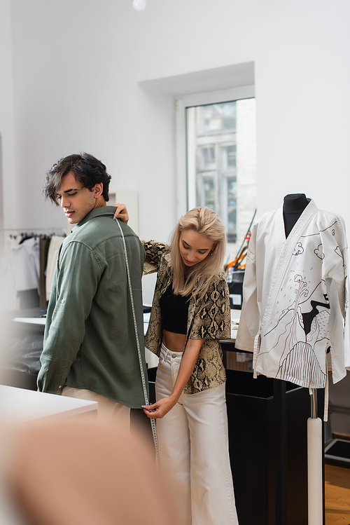 stylish designer measuring size of young man in tailor shop