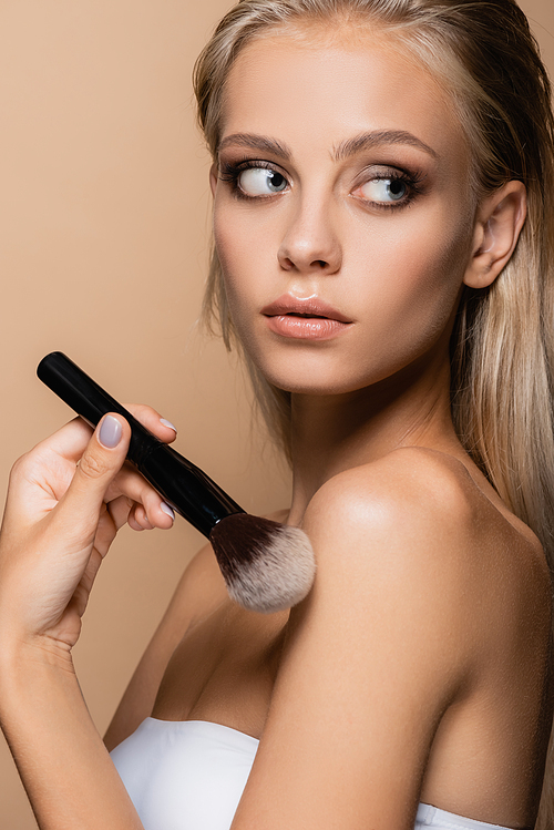 pretty woman with perfect skin touching naked shoulder with soft cosmetic brush isolated on beige