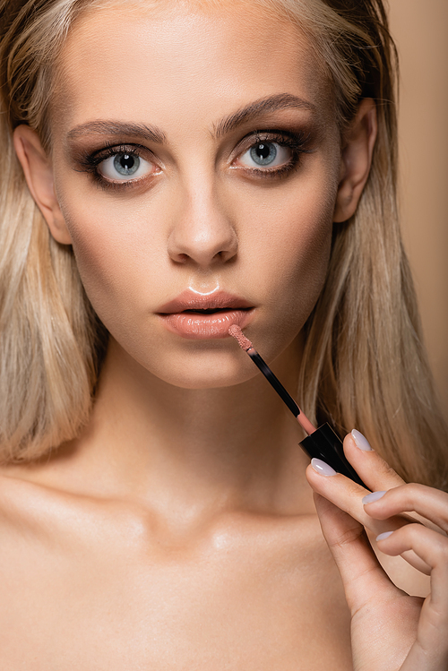 sensual woman with green eyes applying pink lip gloss while  isolated on beige