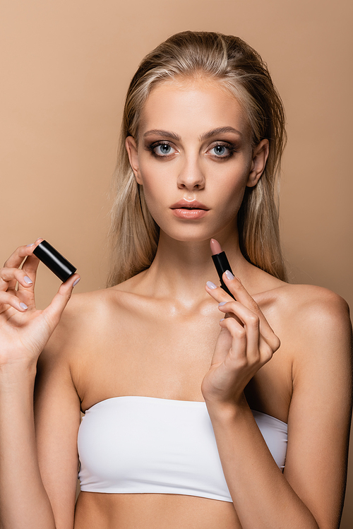 blonde woman with perfect skin holding lipstick isolated on beige