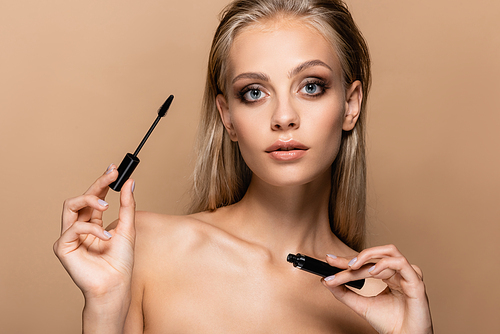 pretty woman with blonde hair and naked shoulders holding black mascara isolated on beige