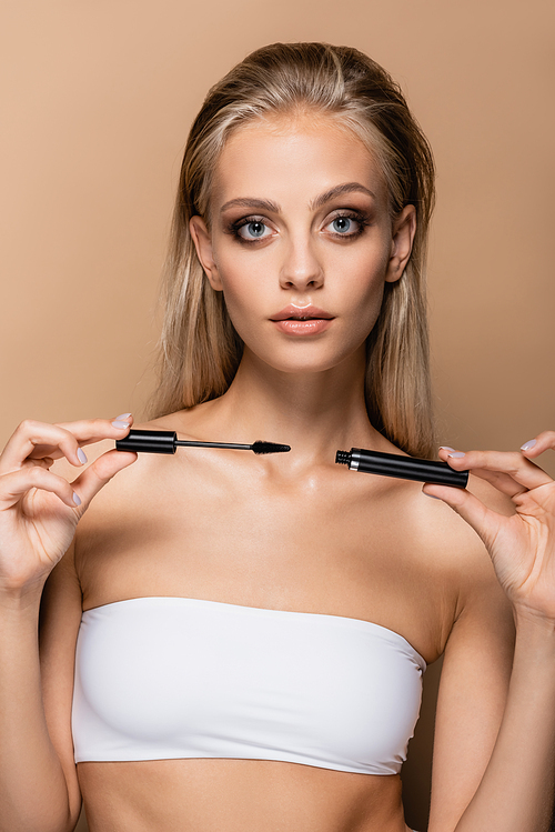 young woman with makeup showing black mascara isolated on beige