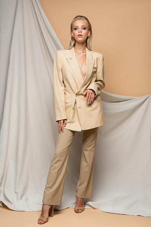 pretty woman in stylish suit  near drapery on beige background