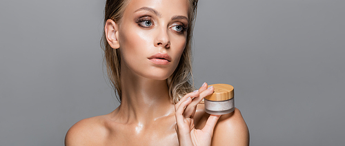 wet woman holding cosmetic cream near bare shoulder isolated on grey, banner