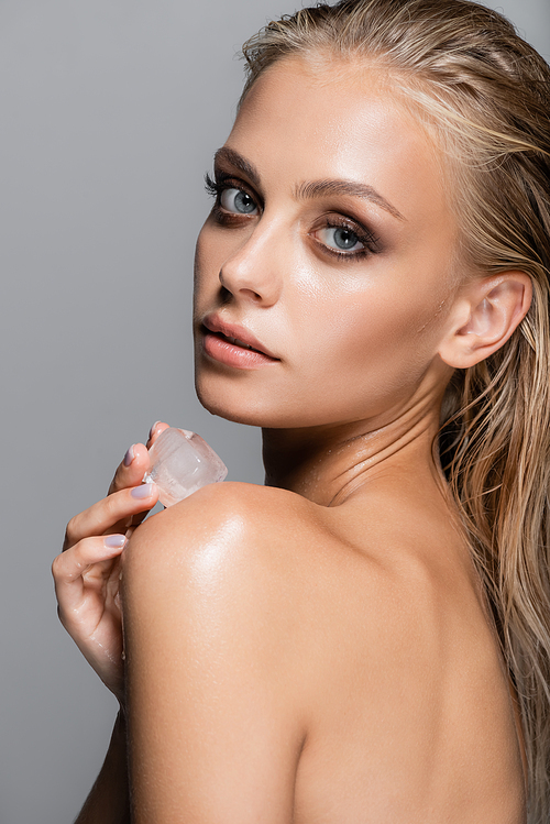 sensual woman touching bare shoulder with ice cube isolated on grey