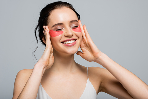 Smiling woman with eye patches touching face isolated on grey