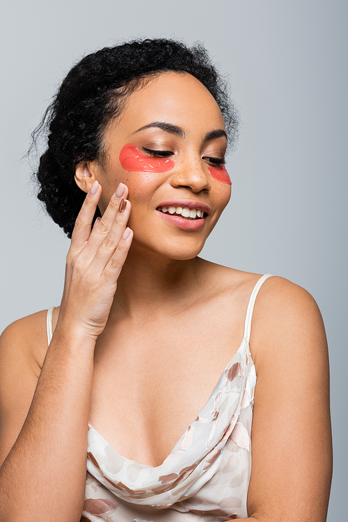 Smiling african american woman in eye patches touching cheek isolated on grey