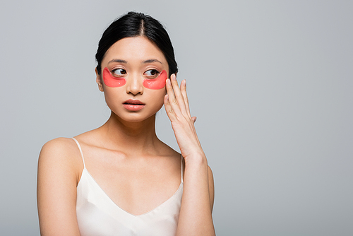 Pretty asian woman touching eye patch on face isolated on grey