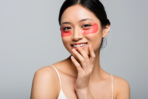 Pretty asian woman with eye patches smiling at camera isolated on grey