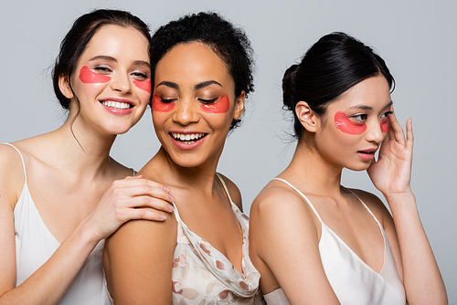 Smiling woman with eye patches standing near multiethnic friends isolated on grey