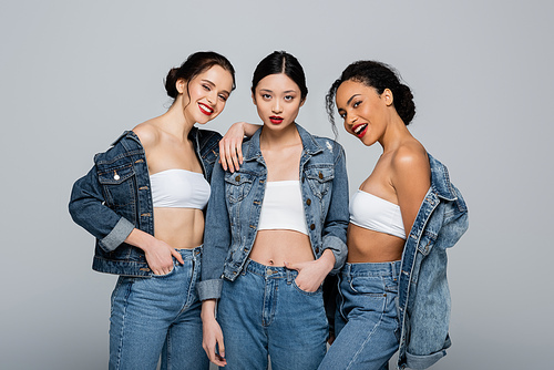 Smiling interracial women in denim jackets  isolated on grey