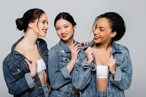 Pretty multicultural women with red lips looking at each other isolated on grey