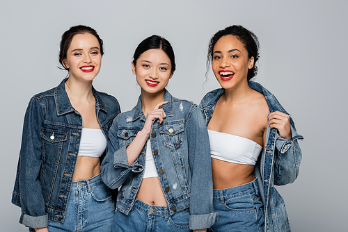 Asian woman with red lips smiling near interracial friends in denim jackets isolated on grey