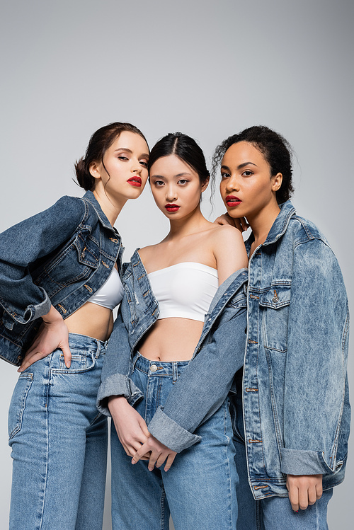 Low angle view of young interracial women in denim jackets  isolated on grey