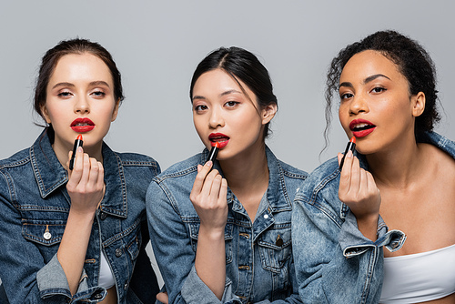 Pretty multicultural women applying red lipsticks and  isolated on grey