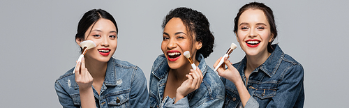 Pretty multiethnic women with red lips holding cosmetic brushes and  isolated on grey, banner