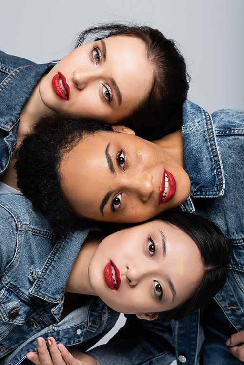 Young interracial women with red lips and face foundation  isolated on grey