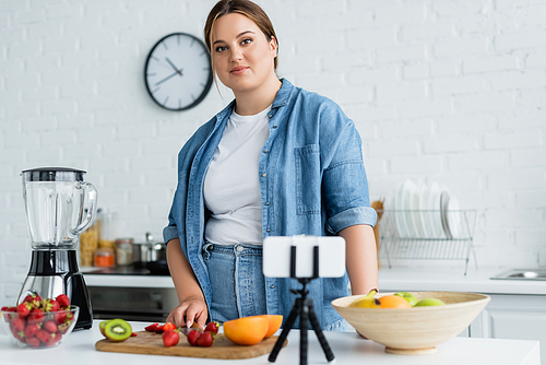 Plus size woman  near blurred smartphone and ripe fruits in kitchen