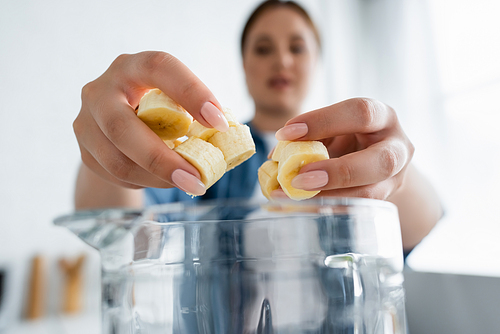 Blurred woman holding sliced banana near blender in kitchen