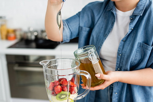 Cropped view of plus size woman pouring honey in blender with fruits